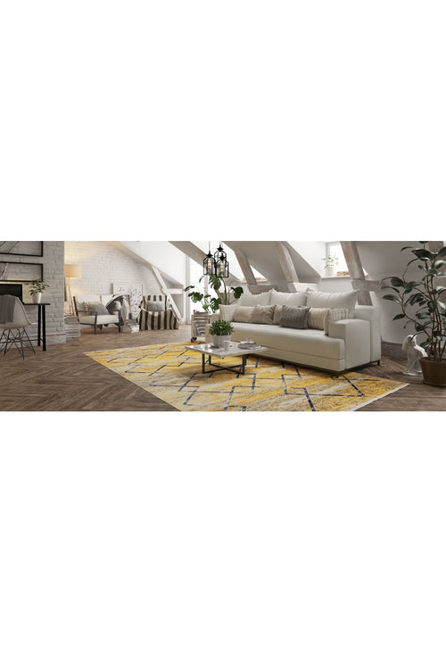 Load image 1 in gallery view. A cozy attic living room with exposed beams, a white sofa, a wooden coffee table, potted plants, natural light, and the Crossed Connections - Washable Rug - JR1181 (Outlet) US in yellow-gold—ideal for high-traffic areas.