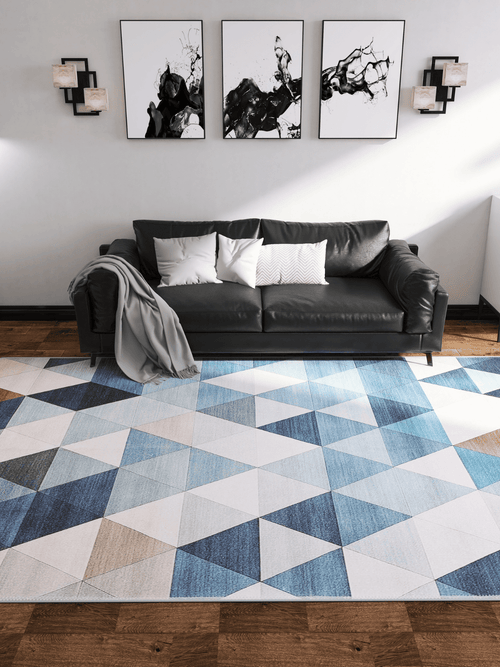 Load image 1 in gallery view. A modern living room with a black sofa, white and gray pillows, a gray throw, and the Cubism Collage Blue Washable Rug - MDJ008 (Custom Size), ideal for high-traffic areas. Three abstract artworks and two wall lights hang above the sofa on wooden flooring.