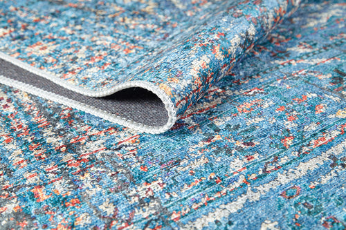 Load image 1 in gallery view. A close-up of the Desert Diamond - Washable Rug - JR5071 (Custom Size) showcases its colorful blue, red, and white patterns. One corner is folded to reveal a gray underside and detailed edge stitching—durable and easy to clean for high-traffic areas.