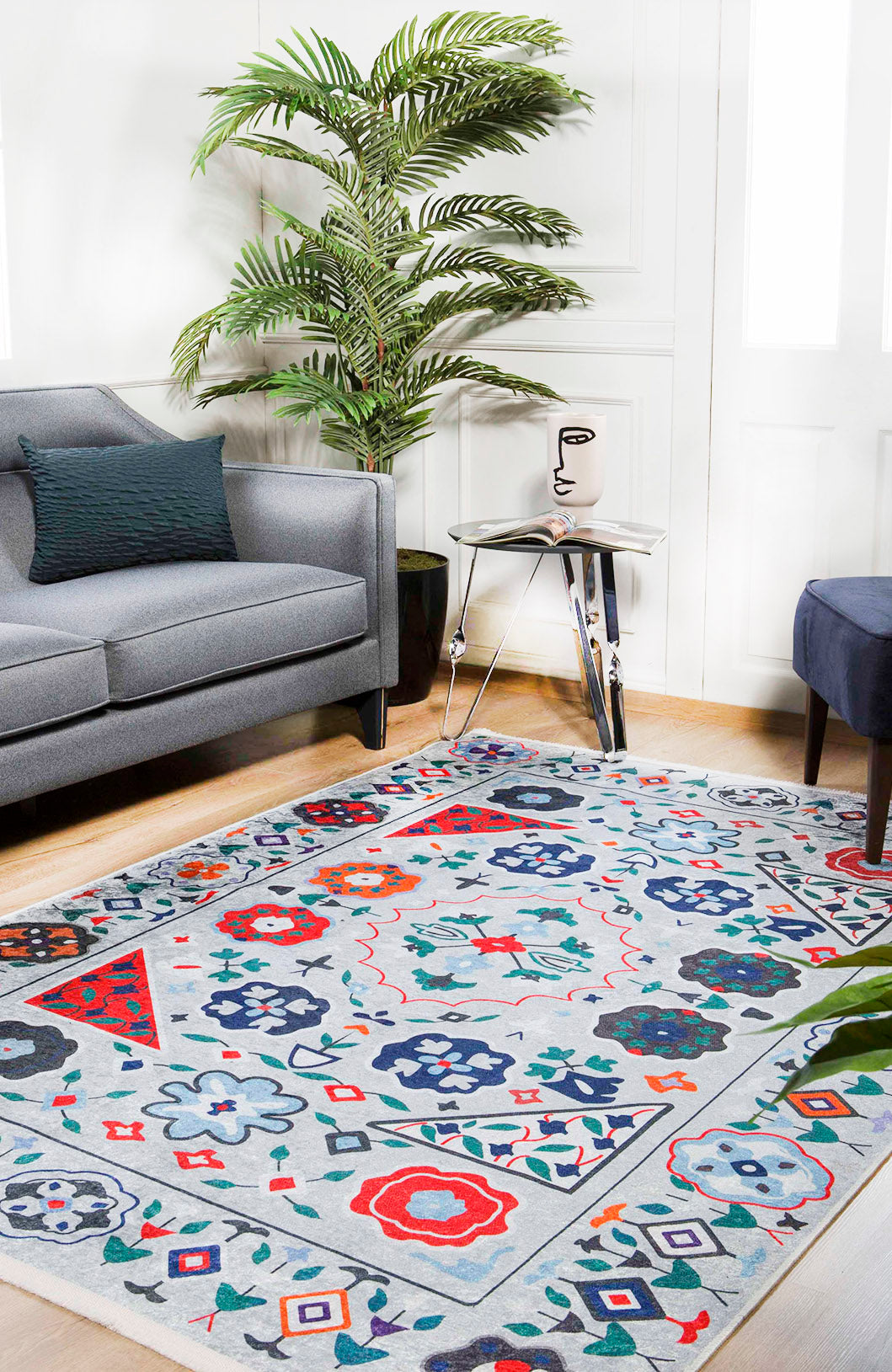 A modern living room with a gray sofa, decorative plant, glass side table with an abstract face vase, and the Desert Drift - Washable Rug - JR1523 (Custom Size)—perfect for high-traffic areas—on a light wooden floor.