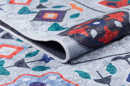 Bild 1 in Galerieansicht laden. A close-up of the Desert Drift - Washable Rug - JR1523 (Custom Size) shows its vibrant abstract geometric and floral patterns on a light gray background. The folded corner reveals detailed texture and stitching, ideal for high-traffic areas.