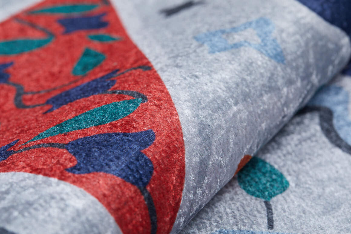A close-up of Desert Drift - Washable Rug - JR1523 (Custom Size) shows abstract red, blue, teal, and gray shapes on a soft, velvety surface with bold patterns—perfect for high-traffic areas.
