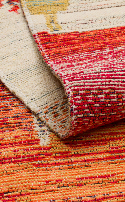 Load image 1 in gallery view. A close-up of the Dust Trace - Kilim - NMD12 rug with a folded corner, showcasing its vibrant red, orange, yellow, and cream hues in a textured, patterned modern design.
