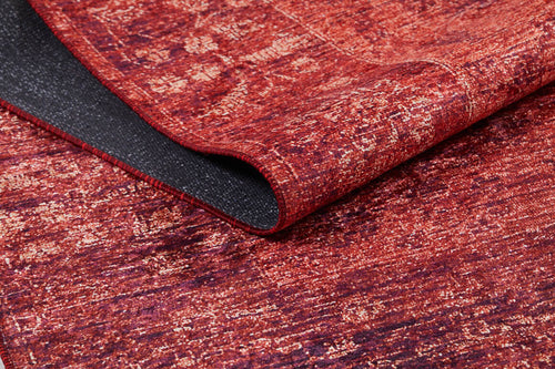Load image 1 in gallery view. The Dynasty Dream - Washable Rug - JR160 (Custom Size) features a textured, slightly distressed red and orange abstract oriental pattern. A folded corner reveals its black non-slip backing, combining style with practical washability.