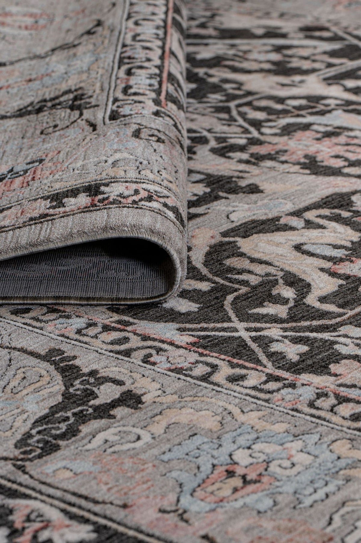Charcoal, grey, and muted pink traditional floral medallion rug with a folded corner showing the pile and backing.