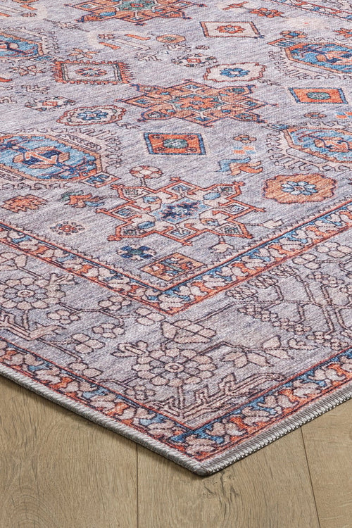 Load image 1 in gallery view. A close-up of the Echelon Bordered Washable Rug - LCC3018, featuring an intricate geometric and floral pattern in blue, orange, and cream on a light wood floor—ideal for high-traffic areas.