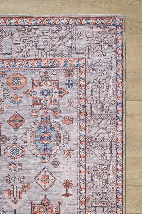 Load image 1 in gallery view. The Echelon Bordered Washable Rug - LCC3018, featuring geometric and floral patterns in blue, orange, and ivory, is perfect for high-traffic areas—only its corner is visible on a light wood floor.