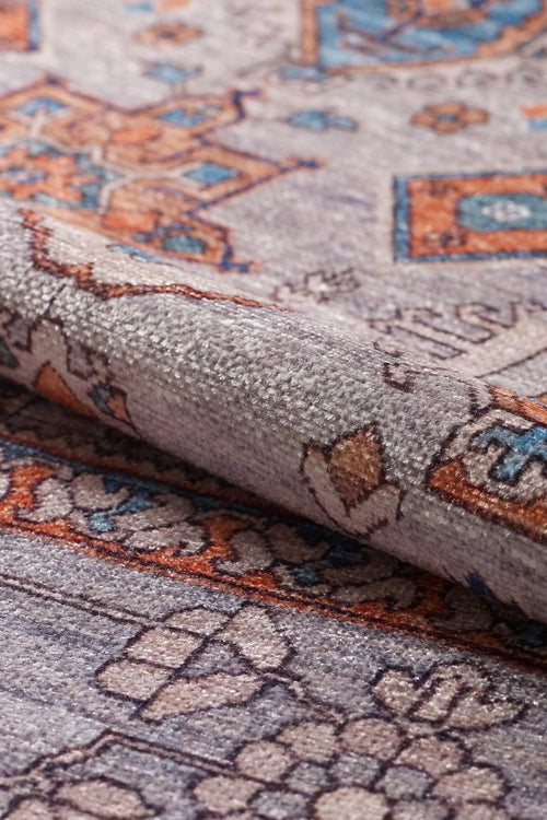 Load image 1 in gallery view. A close-up of the Echelon Bordered Washable Rug - LCC3018, featuring intricate geometric and floral designs in grey, orange, and blue hues; perfect for high-traffic areas with a slightly folded edge shown.