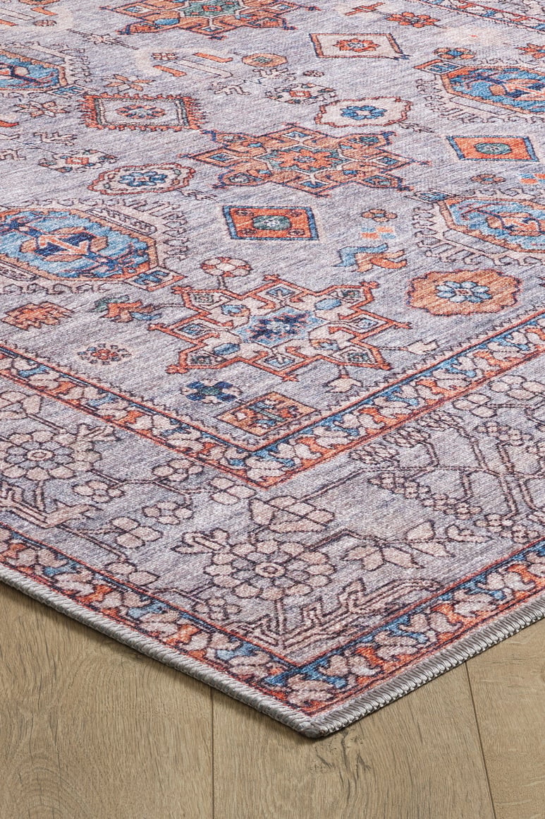 A close-up of the Echelon Bordered Washable Rug - LCC3018 (Custom Size) featuring geometric and floral patterns in blue, orange, and ivory on beige, ideal for high-traffic areas and shown on a wooden floor.