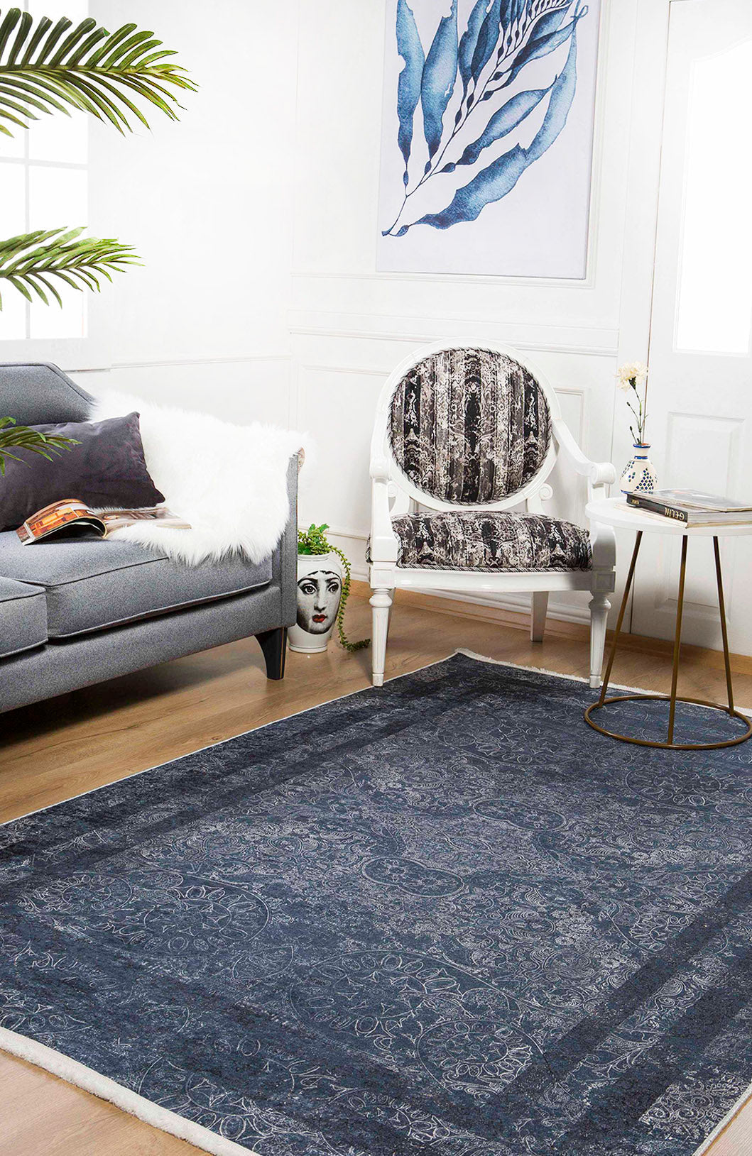 A stylish living room featuring a gray sofa, white fur throw, artistic chair, round side table with vase, large Elegant and Modern - Washable Rug - JR1297 (Custom Size) ideal for high-traffic areas, decorative face planter, and blue leaf wall art.