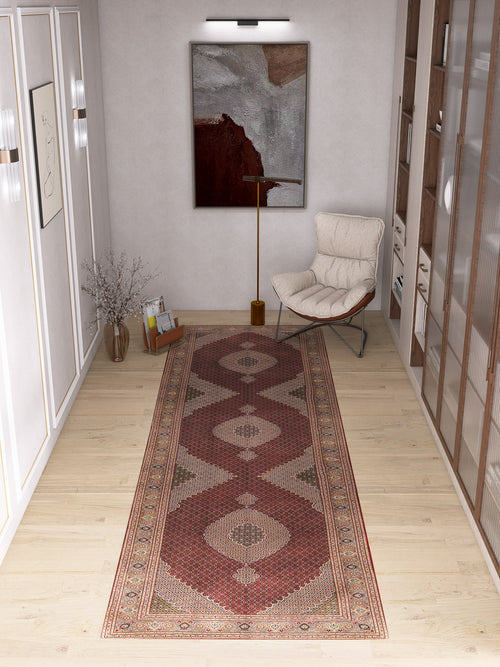 Bild 1 in Galerieansicht laden. A modern hallway with light wood flooring showcases the Elysian Weave - Washable Rug - JRN1001 in red tones, a medallion design, an abstract wall painting, a cream lounge chair with a gold floor lamp, and a glass vase of dried branches.