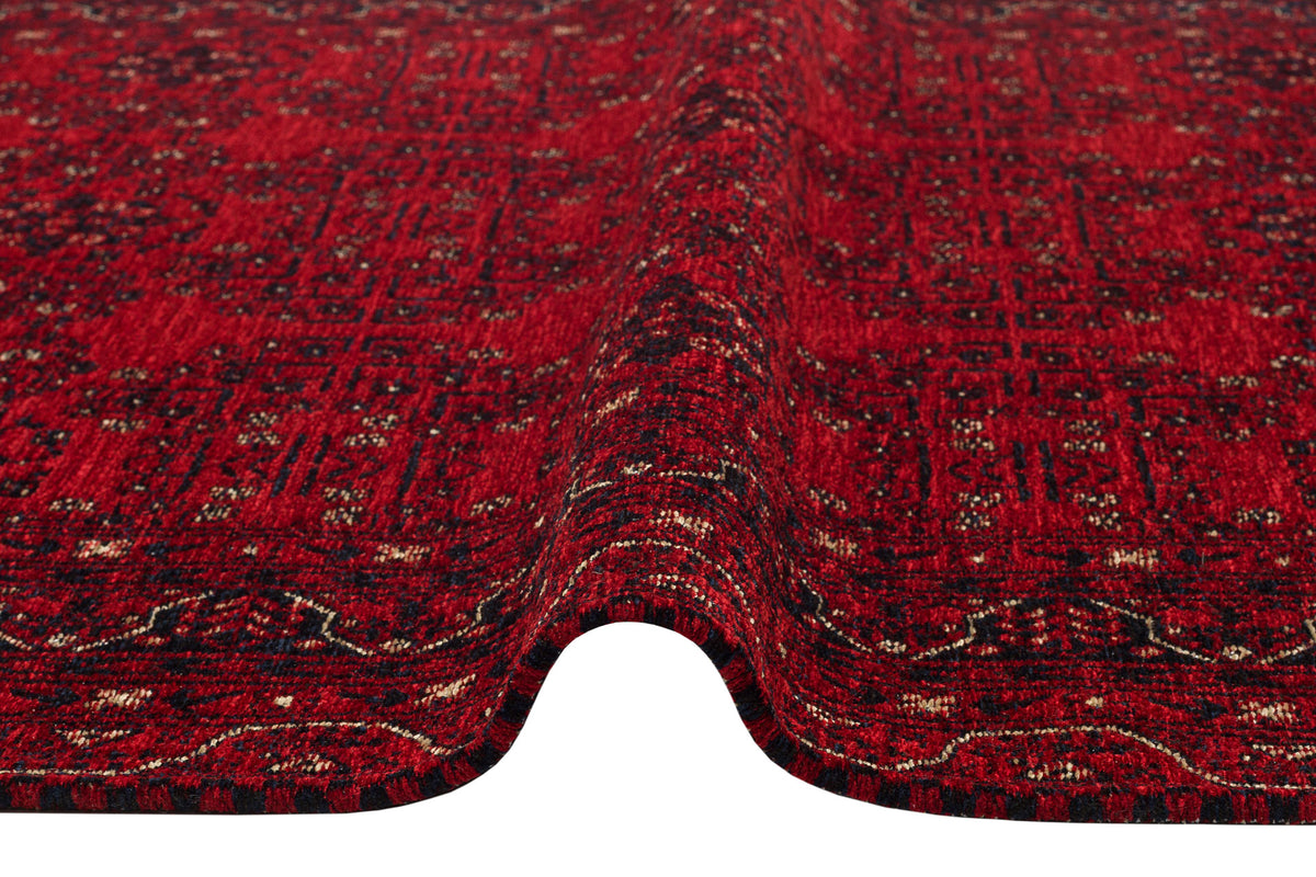 A close-up of the Ember Stitch - Washable Kilim - BHR02 shows its red surface with intricate black and white geometric patterns and borders, featuring a gentle wave or crease through the center.