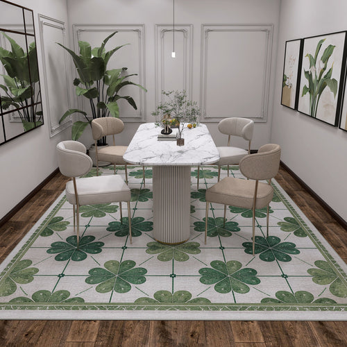 Load image 1 in gallery view. A modern dining room with a marble table, four beige chairs, green plants, wall art, and a wooden floor topped with the Emerald Charm - Washable Rug - JRS013 (Custom Size) featuring a green four-leaf clover pattern. Minimal, bright lighting.