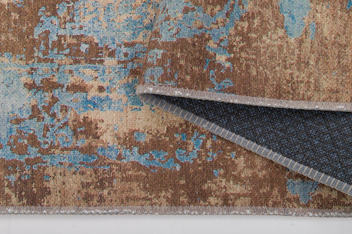 Load image 1 in gallery view. A close-up of the Enchanted Threads - Washable Rug - JRS002 (Outlet) US displays its brown, beige, and blue abstract pattern, textured flat weave, and a flipped corner revealing a dark non-slip backing—highlighting its practicality.