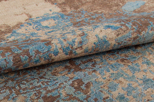 Load image 1 in gallery view. Close-up of the Enchanted Threads - Washable Rug - JRS002 (Custom Size), featuring a folded, textured surface with an abstract blue and brown pattern on beige. Its vintage, weathered look is perfect for allergy-sensitive homes and high-traffic areas.