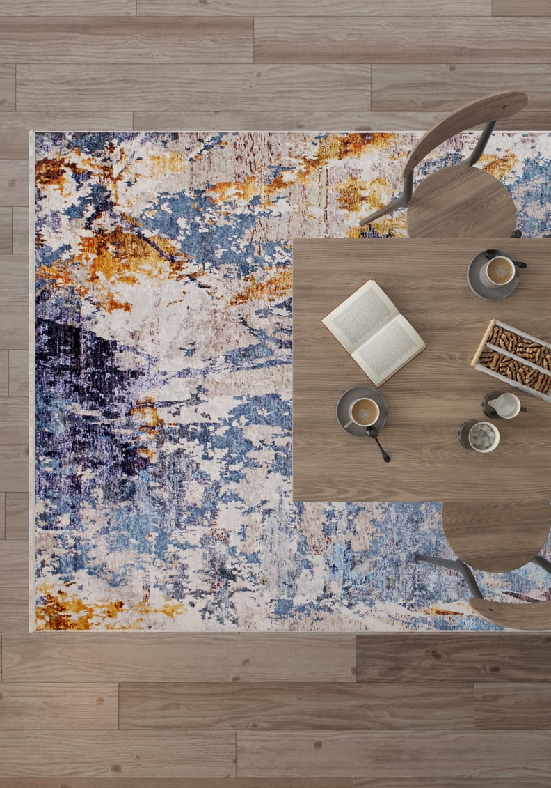 Overhead view of a wooden table for two with snacks, coffee, and an open book on the Enigmatic Elegance - Washable Rug - JR787, featuring abstract blue patterns—perfect for high-traffic areas atop a wooden floor.