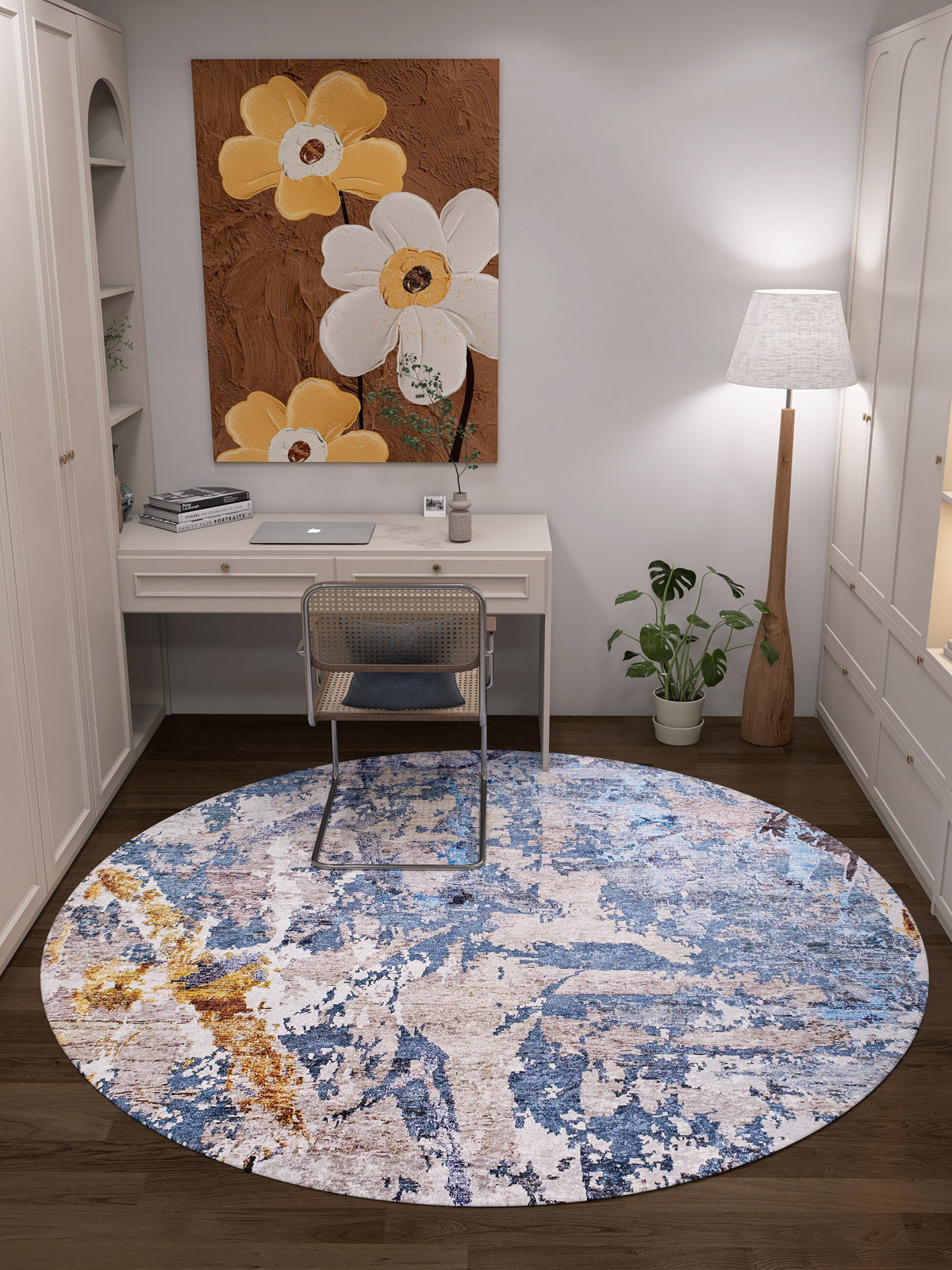 A cozy home office features a white desk, chair, books, computer, and a large yellow and white flower painting above the desk. The Enigmatic Elegance Washable Rug - JR787 in blue and beige covers the floor—ideal for high-traffic spaces.