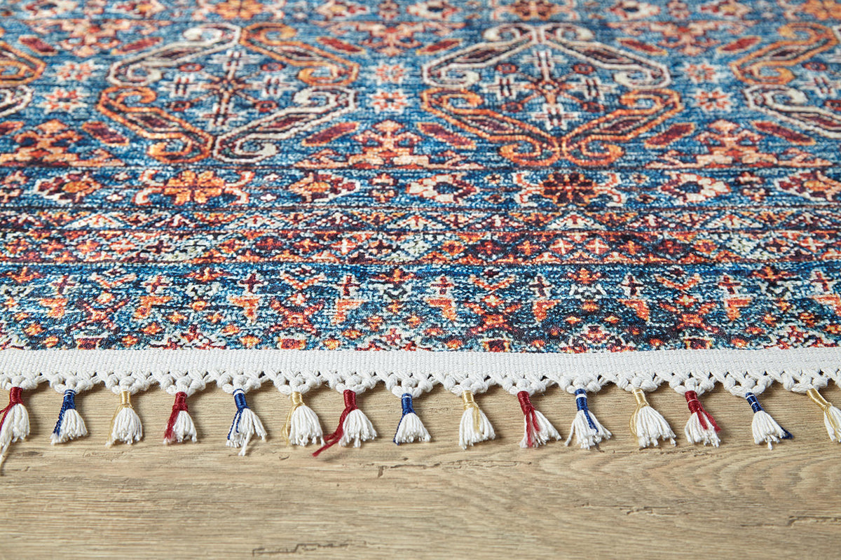 A close-up of the Ethereal Essence - Washable Rug - JR5087 (Custom Size), showcasing intricate blue, red, orange, and white geometric and floral designs with tassels—ideal for high-traffic areas on light wooden floors.