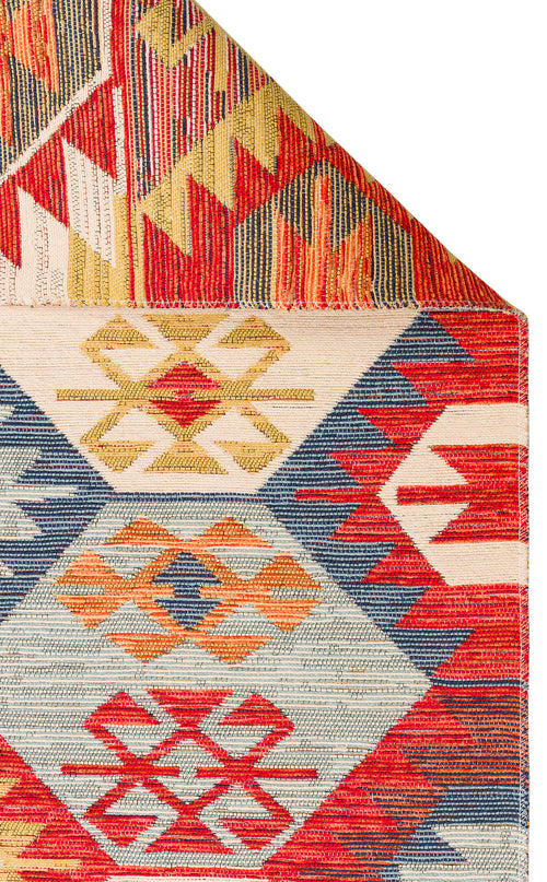 Bild 1 in Galerieansicht laden. Ethnic Mix - Kilim - NMD01: A multicolour rug with geometric diamond and zigzag patterns in red, blue, yellow, and orange; one corner is folded to show vivid tribal motifs beneath.
