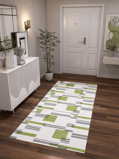 Load image 1 in gallery view. A modern hallway with wood flooring, the Faded Treasure - Washable Rug - JRN46 (Custom Size) in green and black geometric accents, a white sideboard, potted plant, wall art, and a white door—perfect for stylish high-traffic spaces.