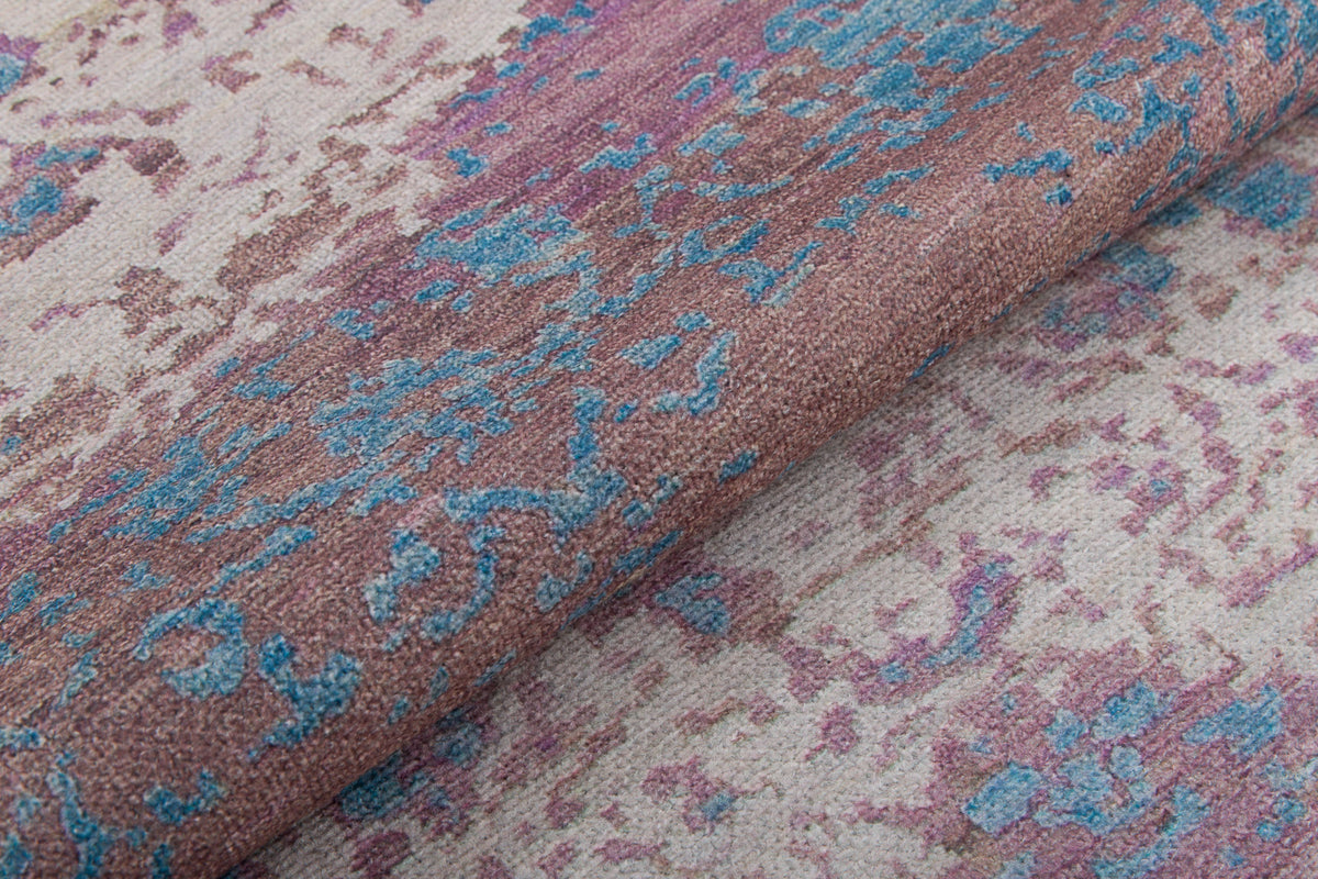 A close-up of the Faerie Weave - Washable Rug (JRS005), featuring a textured, abstract design with mottled brown, beige, pink, and blue tones. Durable and washable, it's ideal for high-traffic areas with its overlapping colors and uneven shapes.