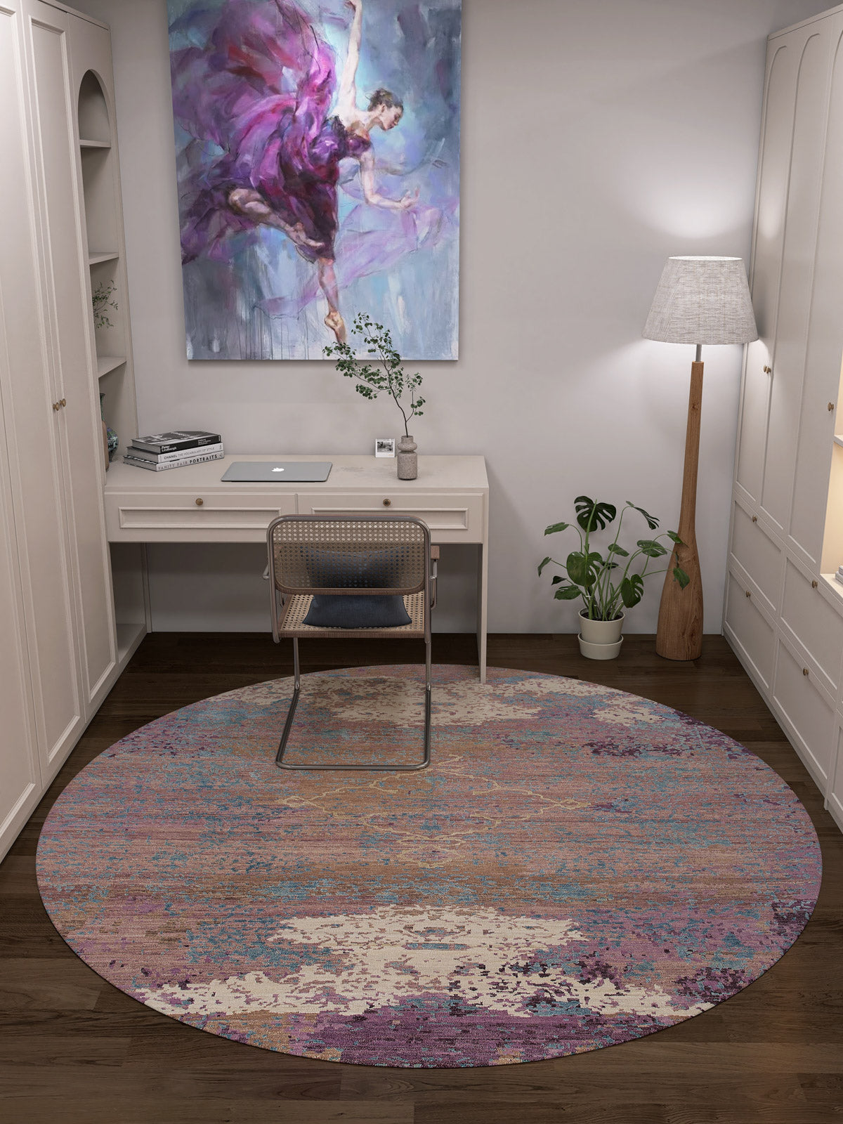 A cozy home office with a white desk, rattan chair, Faerie Weave - Washable Rug - JRS005 (Custom Size) featuring colorful patterns, floor lamp, potted plants, and a painting of a dancer in purple—ideal for high-traffic spaces.