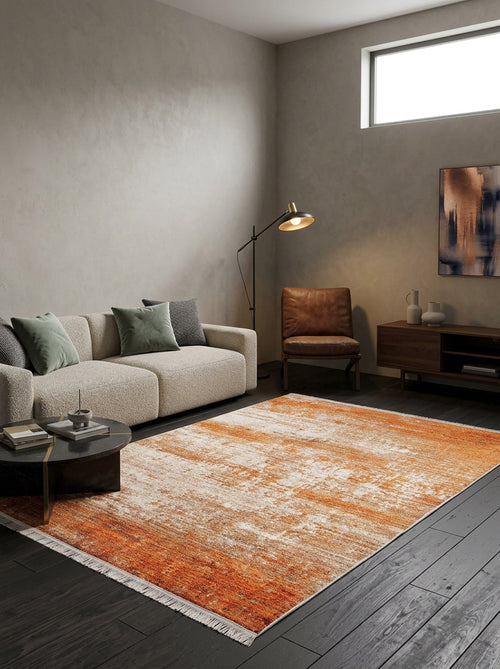 Load image 1 in gallery view. A modern living room features a beige sofa, green and gray pillows, brown chair, standing lamp, coffee table, sideboard, abstract wall art, and the allergy-sensitive Fluffy Brushed - Washable Rug - JR584 in orange on dark wood floors. Light streams in.