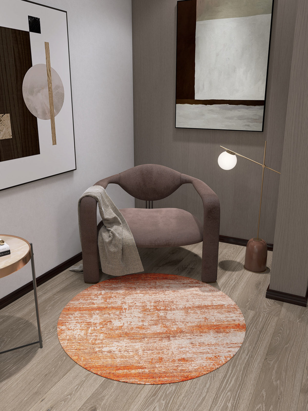 A modern corner featuring a curved mauve armchair with a gray blanket, the Fluffy Brushed Washable Rug - JR584 in orange, a round side table, abstract wall art, and a floor lamp with a white globe shade.