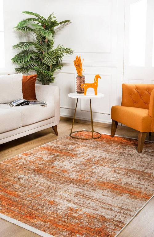 Load image 1 in gallery view. A cozy living room features a beige sofa, orange armchair, round side table with decor, potted plant, and the Fluffy Brushed - Washable Rug - JR584 (Custom Size) in orange on light wood flooring—ideal for high-traffic areas. Sunlit windows brighten the space.