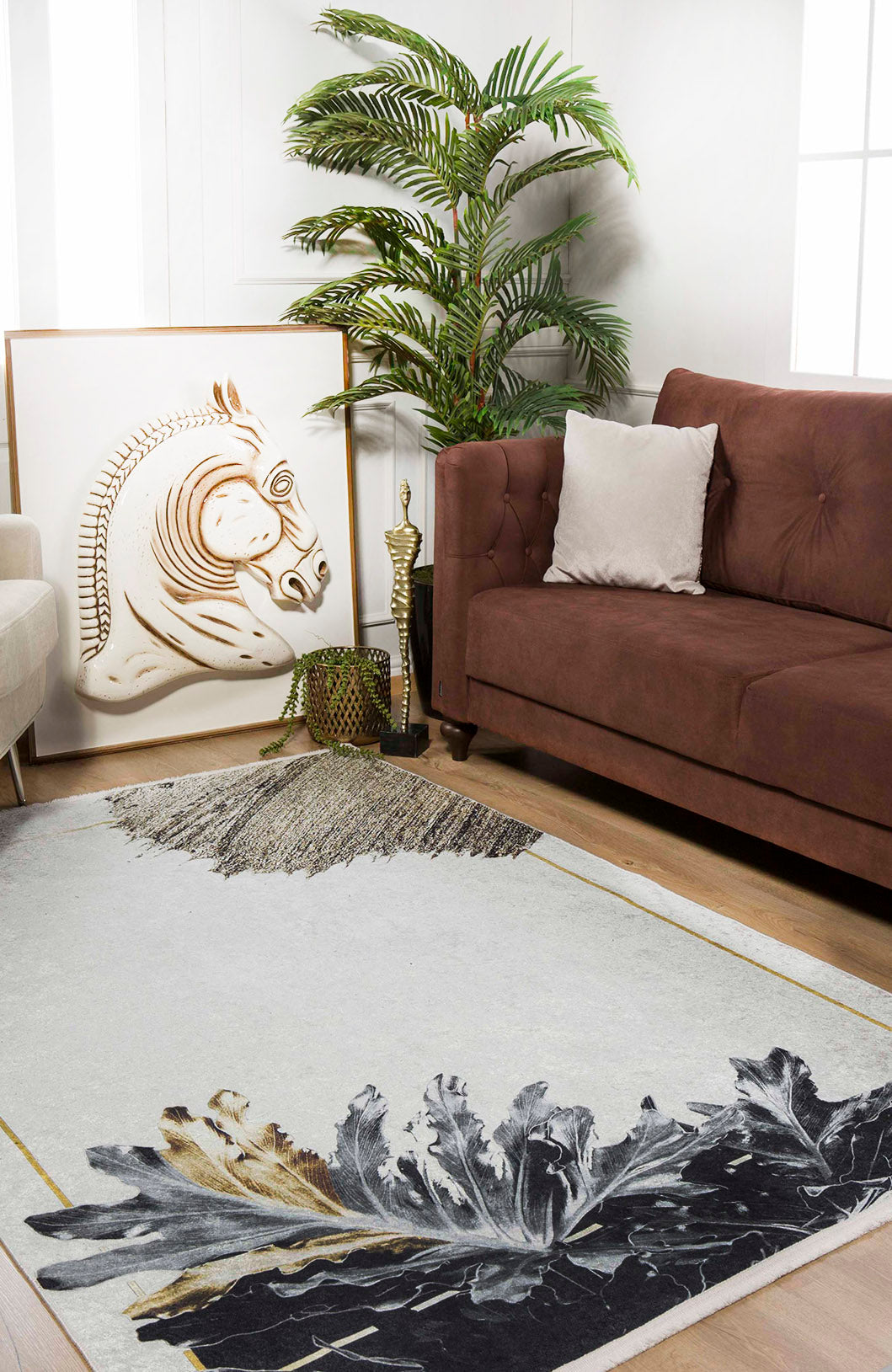 A modern living room features a brown sofa, white pillow, leafy plant, and framed horse art. The Funky Floral Frenzy - Machine-Washable Rug JR1376 (Custom Size) with leafy patterns brightens the wood floor and is perfect for high-traffic areas.