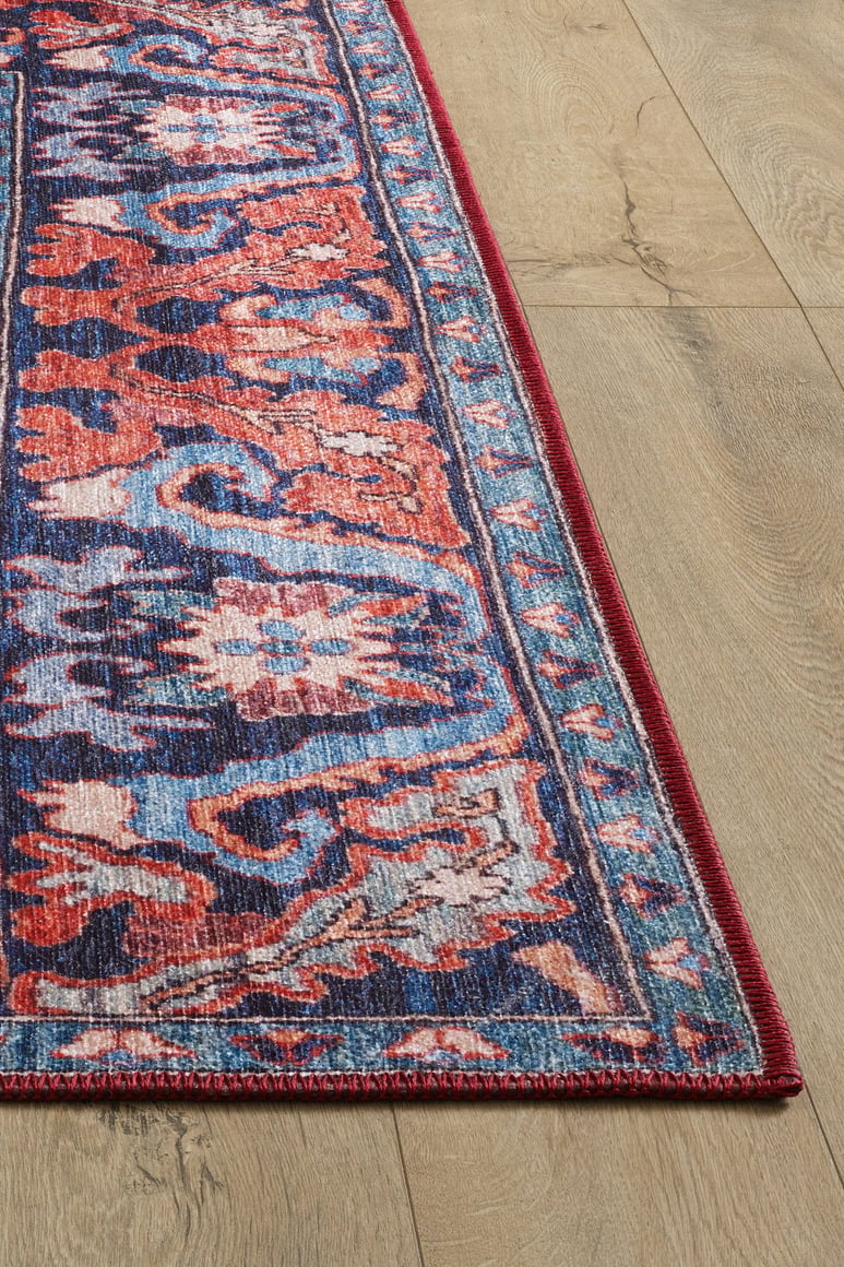 A close-up of the Galea Turkish-Design Coral Washable Rug - LCC3027, showcasing vibrant red, blue, pink, and orange patterns on a light wood floor. Its bold bordered edge makes it ideal for high-traffic areas.