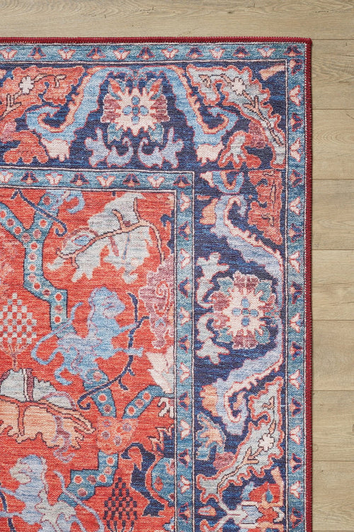 Load image 1 in gallery view. The Galea Turkish-Design Coral Washable Rug (LCC3027), with red, blue, and cream floral and geometric motifs, lies on a light wood floor. Its durable design suits high-traffic areas; only one corner of the rug is visible in the image.