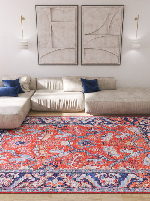 Load image 1 in gallery view. A modern living room with cream sofas, blue accent pillows, abstract art, and the Galea Turkish-Design Coral Washable Rug (LCC3027)—ideal for high-traffic areas—adds vibrant red and blue patterns to a light wood floor.