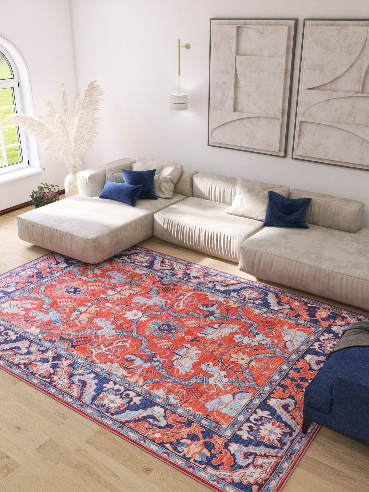 A bright living room with a beige sectional sofa, blue accent pillows, the Galea Turkish-Design Coral Washable Rug—perfect for high-traffic areas—abstract wall art, pampas grass in a vase by the sofa, and natural light streaming through a large window.