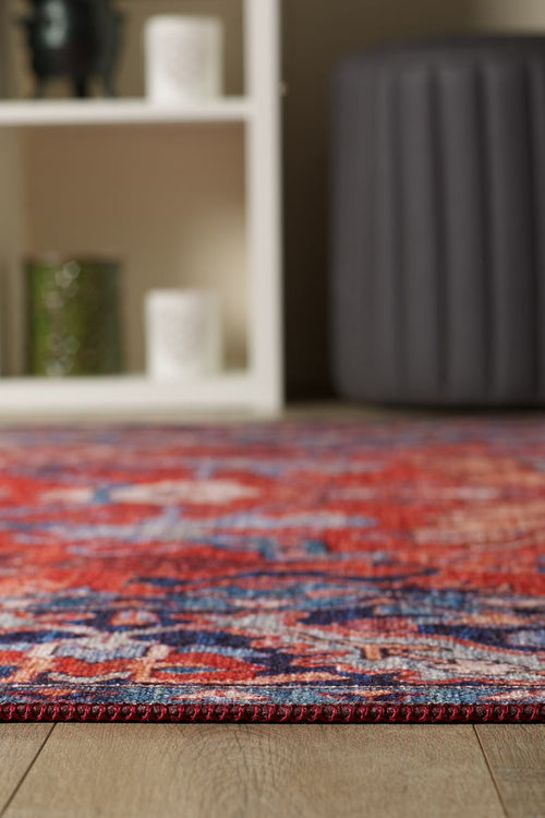 Load image 1 in gallery view. A close-up of the Galea Turkish-Design Coral Washable Rug (LCC3027, custom size) on a wooden floor, perfect for high-traffic areas, with a blurred white decor shelf and a dark gray round ottoman in the background.