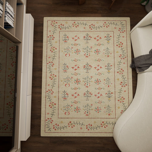 Load image 1 in gallery view. The Garden Cream - Washable Rug - JRN1026 (Custom Size), a rectangular beige rug with a red, green, and blue floral pattern, lies between a white sofa and shelves on a dark wood floor; a gray blanket rests on the sofa’s armrest.