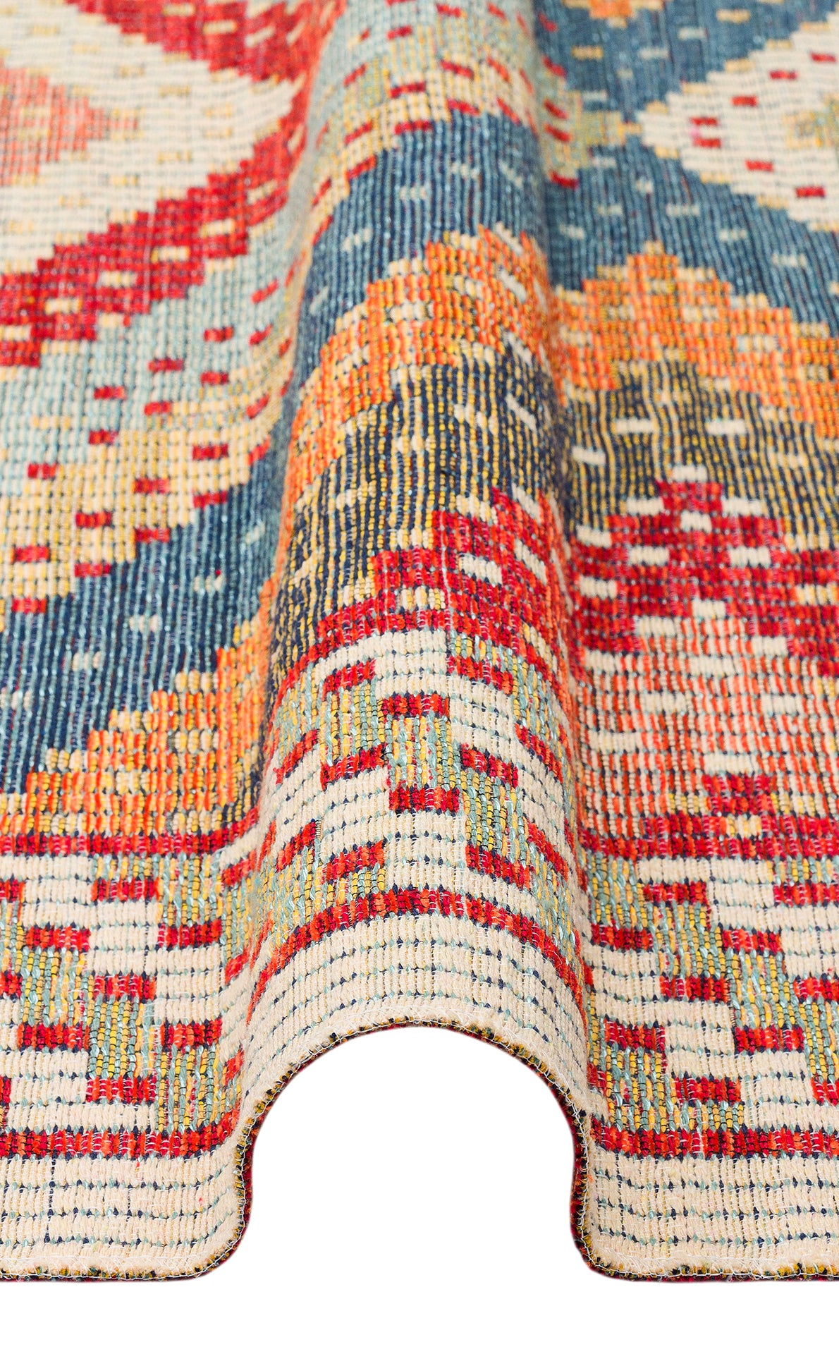 A close-up of the Garnet Print - Washable Reversible Kilim (NMD10), featuring red, blue, orange, and cream geometric patterns. The flatwoven rug is gently lifted in a wave to showcase its intricate texture and design.