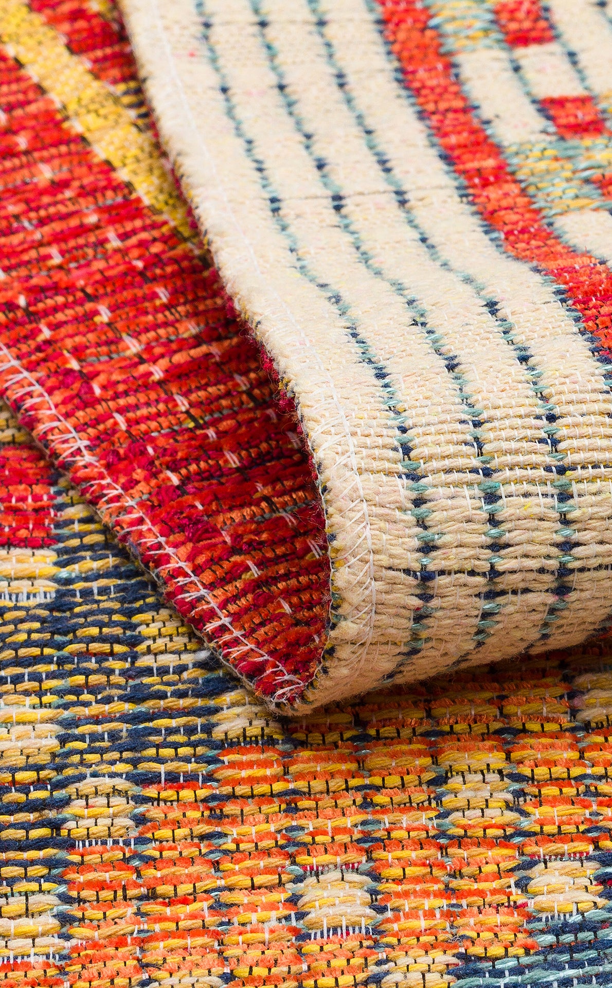 Close-up of the Garnet Print - Washable Reversible Kilim - NMD10, featuring vibrant red, yellow, blue, and cream patterns. The kilim is partially folded to showcase its detailed stitching and front-and-back textures.