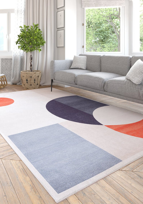Load image 1 in gallery view. A modern living room features a gray sofa, white and gray pillows, a green potted plant, and the Geometric Zen Modern Washable Rug - MDJ002 with blue, orange, and purple shapes—perfect for allergy-sensitive spaces.