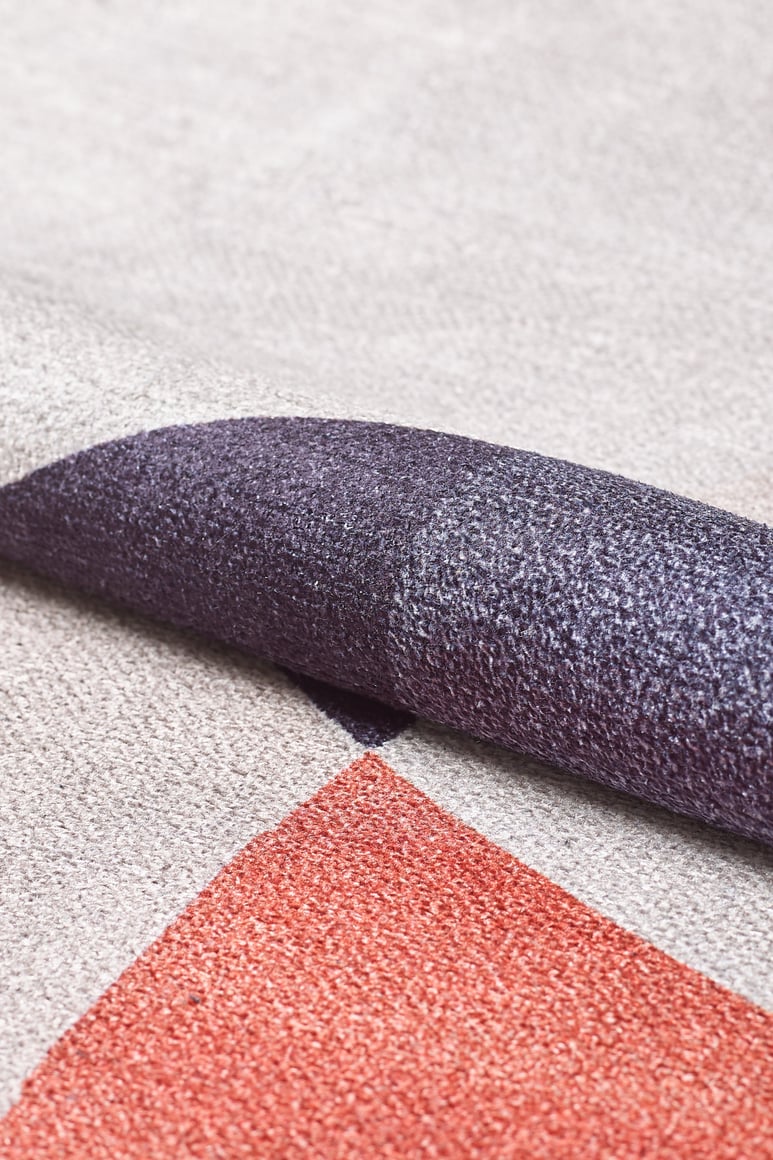 Close-up of the Geometric Zen Modern Washable Rug - MDJ002 (Custom Size) with a folded corner, showcasing a purple, light gray, and reddish-orange color block pattern—ideal for high-traffic areas.