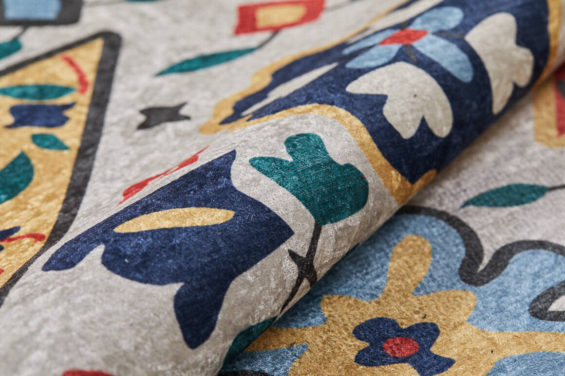 Close-up of the Global Gathering - Washable Rug - JR608 (Custom Size), rolled to display its blue, yellow, green, red, and ivory floral and geometric pattern on a textured light gray background—ideal for high-traffic areas.