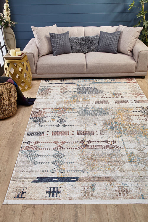 Load image 1 in gallery view. A cozy living room with a beige sofa, gray textured pillows, the Global Glamour Washable Rug - JR1708 (Custom Size) with geometric designs ideal for high-traffic areas, a yellow side table, candles, basket, blanket, plants, and wood floors by a blue wall.