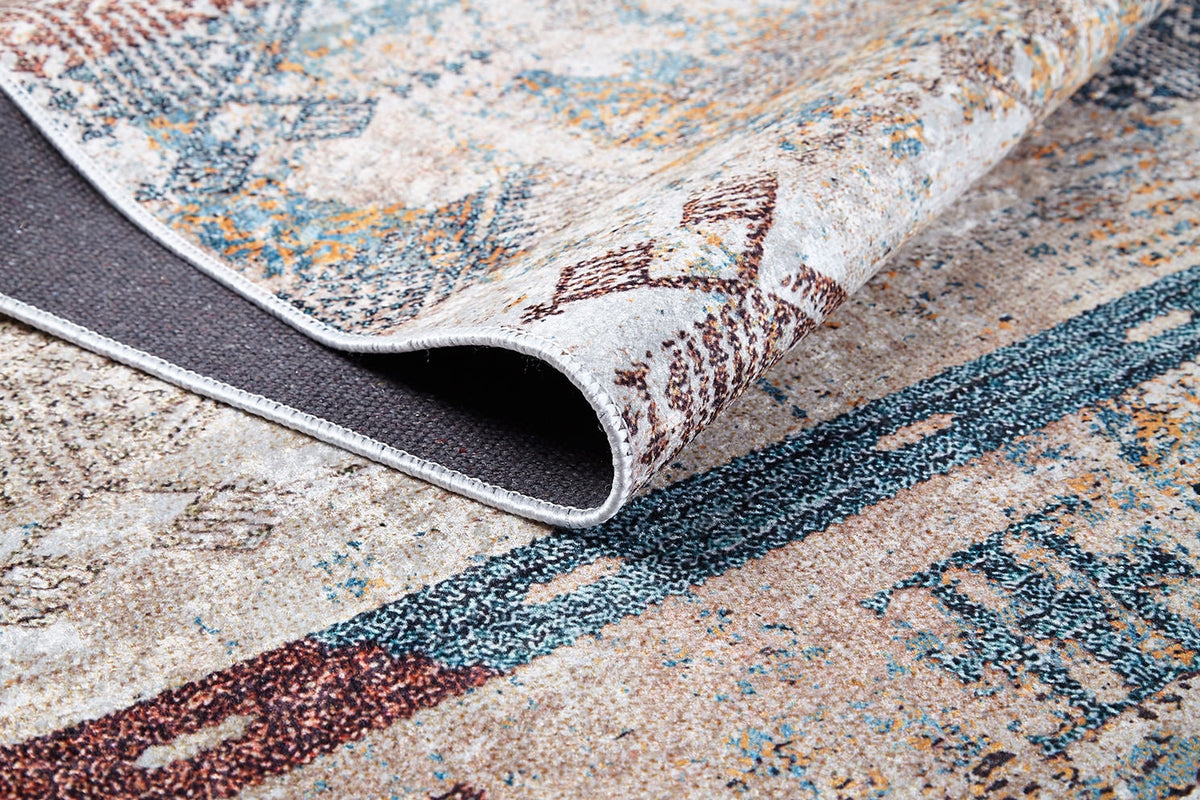 A close-up of the Global Glamour - Washable Rug - JR1708 (Custom Size) with a folded corner shows its textured backing. The rug’s abstract geometric design in earthy tones with blue, brown, and beige suits high-traffic areas.
