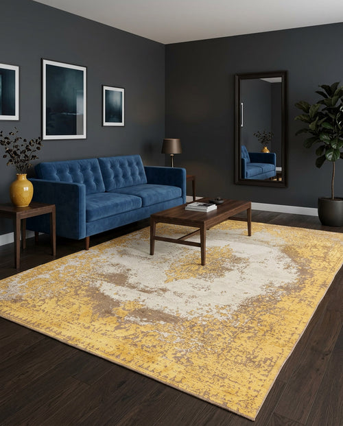 Load image 1 in gallery view. A modern living room with a dark blue sofa, wooden coffee table, the Golden Fade Area Rug APX1922 in yellow and beige, wall art, tall mirror, potted plant, and dark walls and flooring.