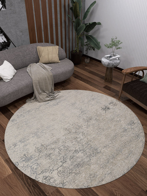 Load image 1 in gallery view. A modern living room features the Graceful Tapestry - Washable Rug - JR1975 on dark wood floors, a curved gray sofa with cushions and a throw, a wooden chair, a side table with a plant, and a tall houseplant in the corner.