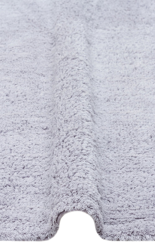 Load image 1 in gallery view. Close-up of the Grey Snug - Washable Shaggy - CBNPLAIN rug in light gray, featuring a soft, plush texture and a visible raised fold running vertically through the center.