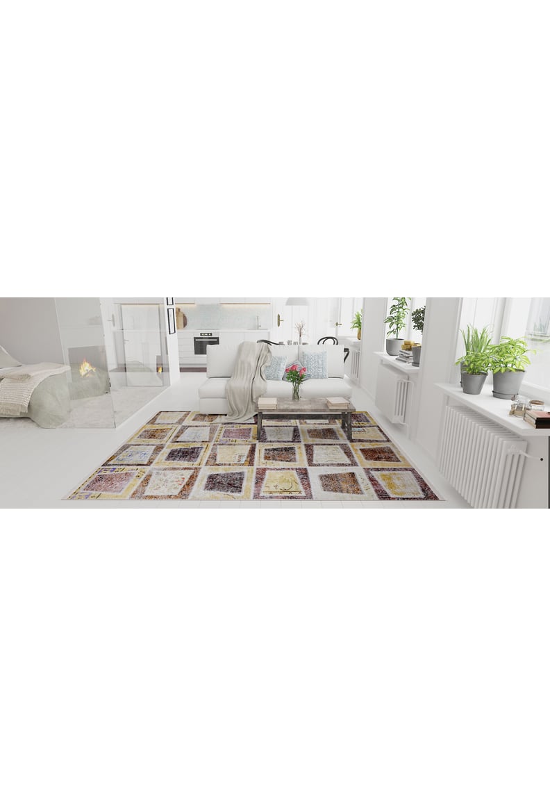 A bright, modern living room with white walls, a large window, houseplants on the sill, a Gridiron Glow - Washable Rug - JR183 perfect for high-traffic areas, a glass coffee table with flowers, and a cozy sofa draped with a throw blanket.