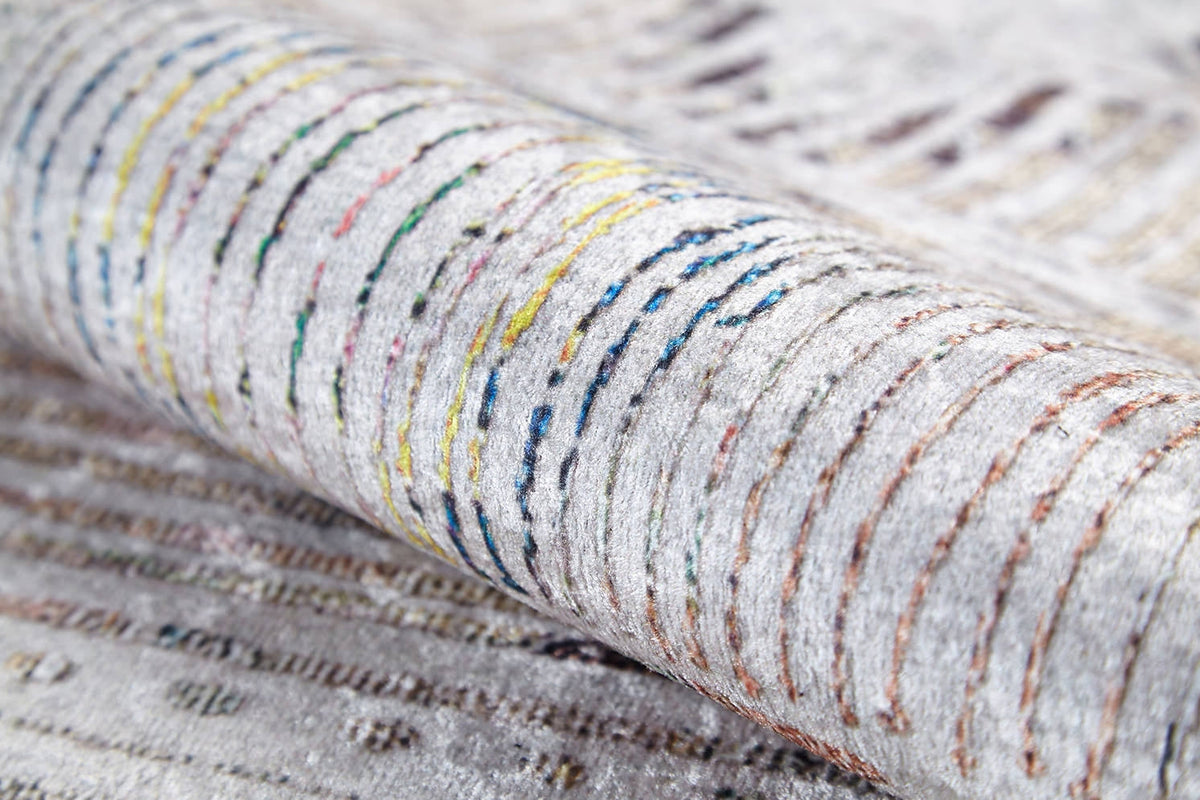 A close-up of the Gypsy Glam - Washable Rug - JR1716 (Custom Size), showcasing its soft, plush white and gray base with colorful curved and straight stitched lines in yellow, blue, green, orange, and brown.