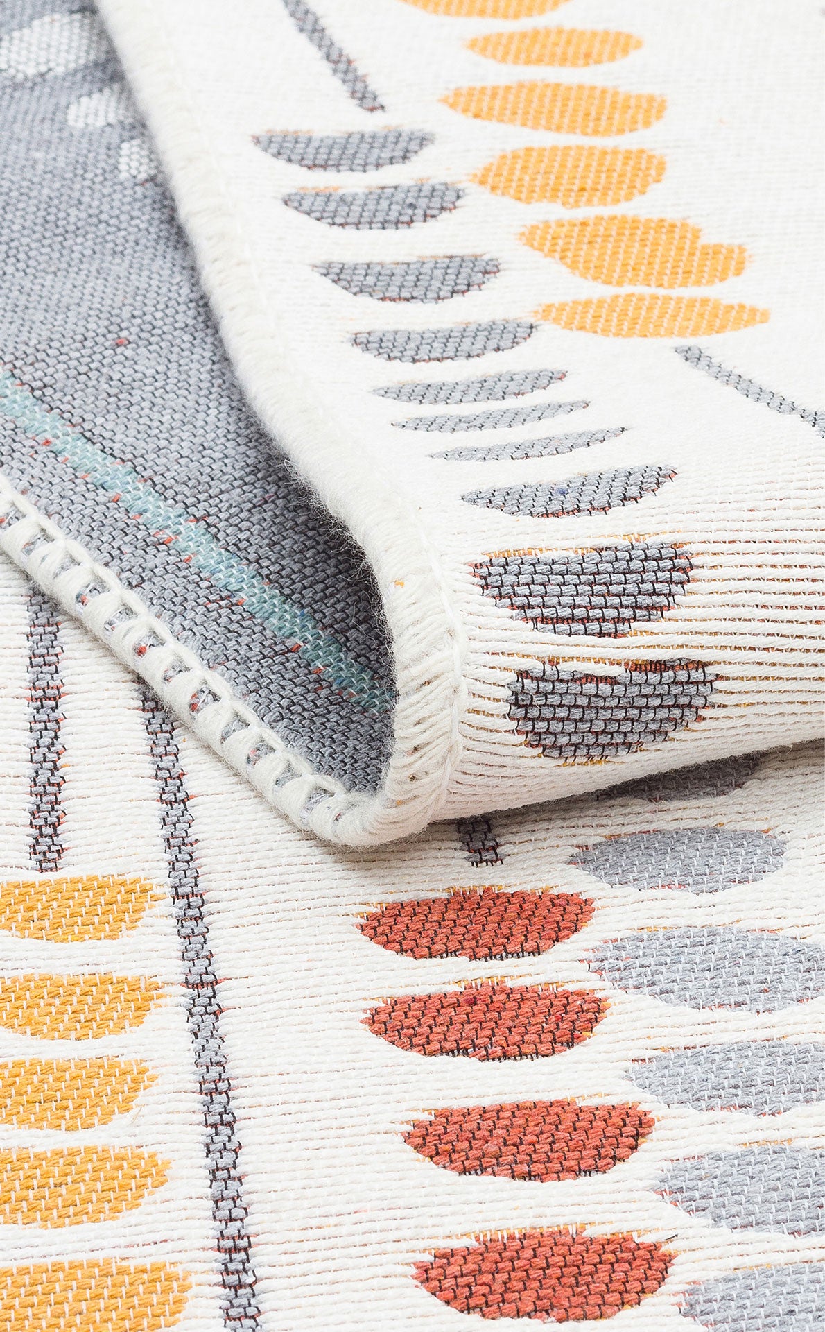 A close-up of the Harmony Weave - Washable Reversible Kilims - AR34 shows a folded corner, with gray, yellow, and orange oval rows on cream. Its texture and stitching reflect contemporary style and quality craftsmanship.