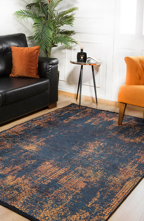 Load image 1 in gallery view. A cozy living room with a black sofa, orange pillow, orange armchair, the Hushed Tones - Washable Rug - JR1428 (Custom Size) in dark blue and orange for high-traffic areas, a small round side table with decor, and a potted plant in the corner.